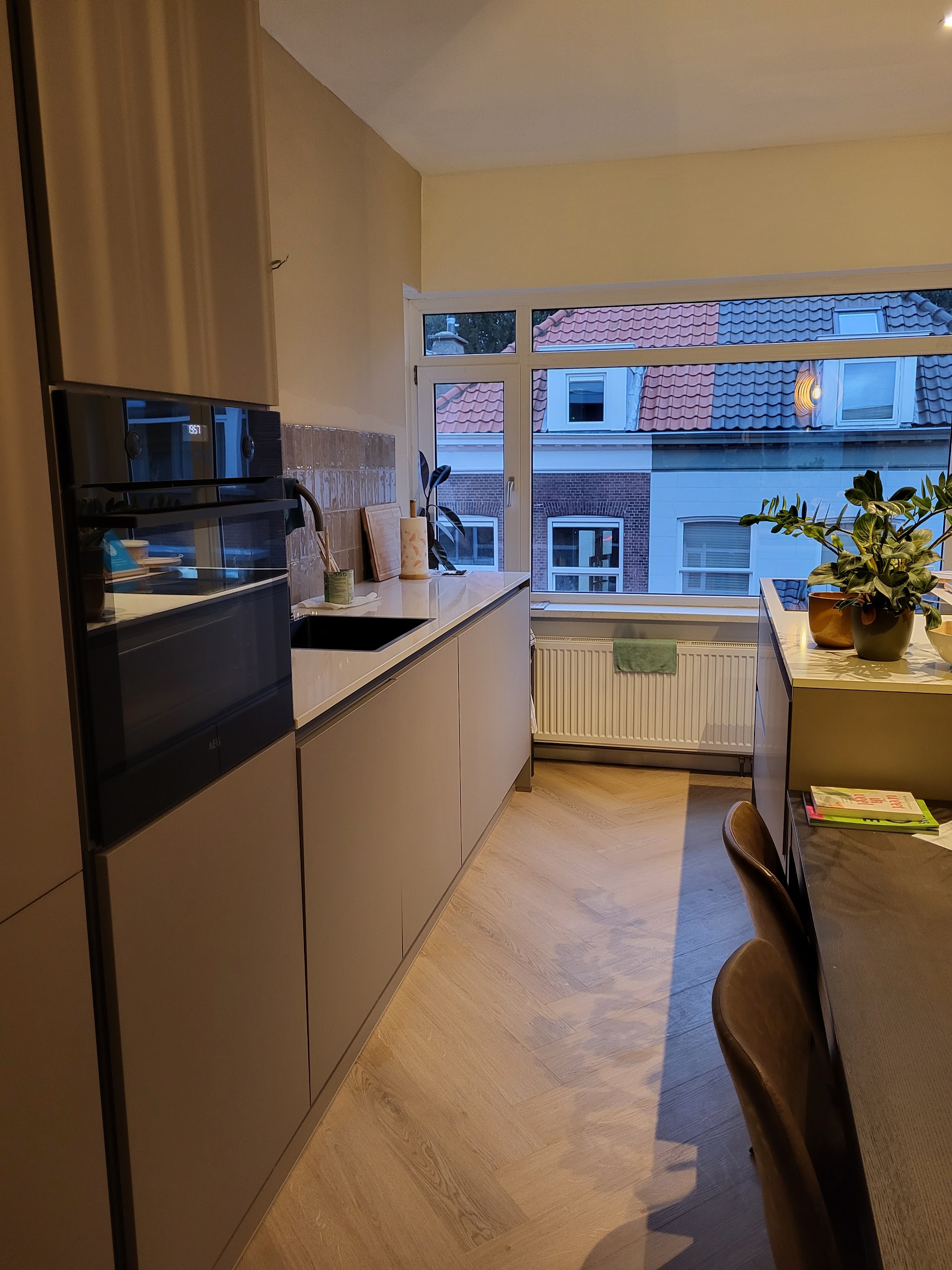 Lange greige keuken met hoge ovenkast en een raam aan het eind