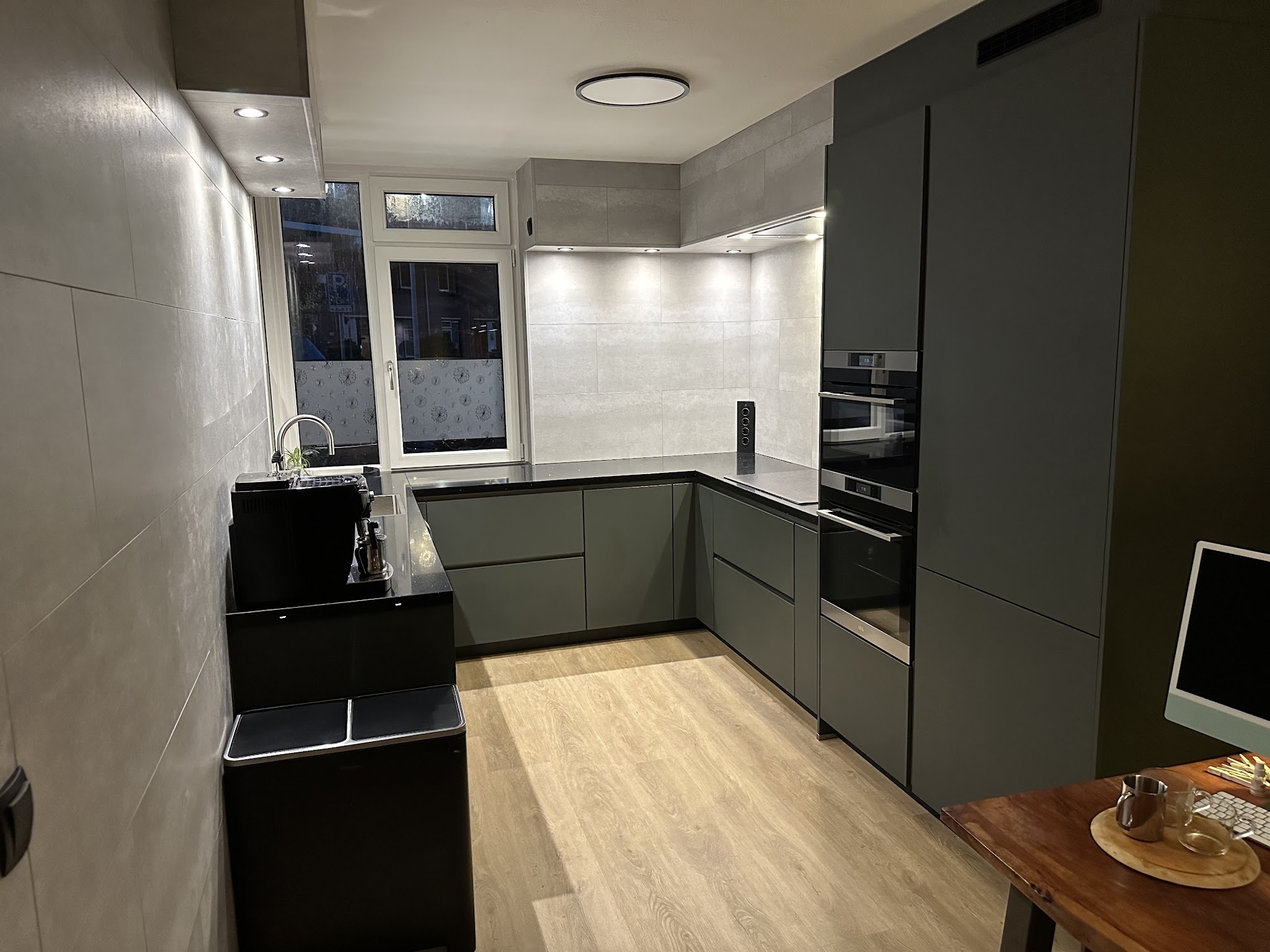 Donkere U-keuken met hoge ovenkast, betegelde wand en een verlichte nis
